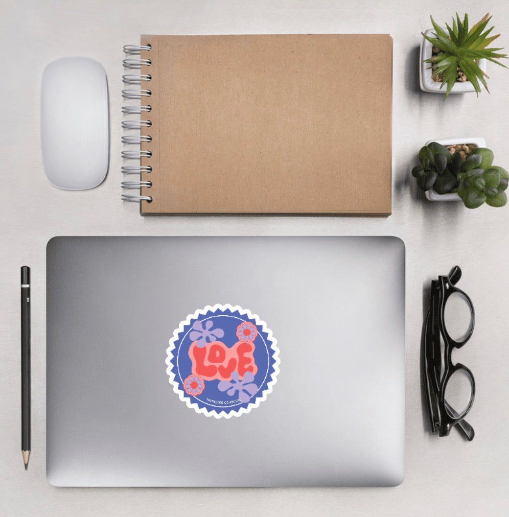Aerial view of laptop with a sticker with 'LOVE' text and floral designs, with a background of desk accessories 
