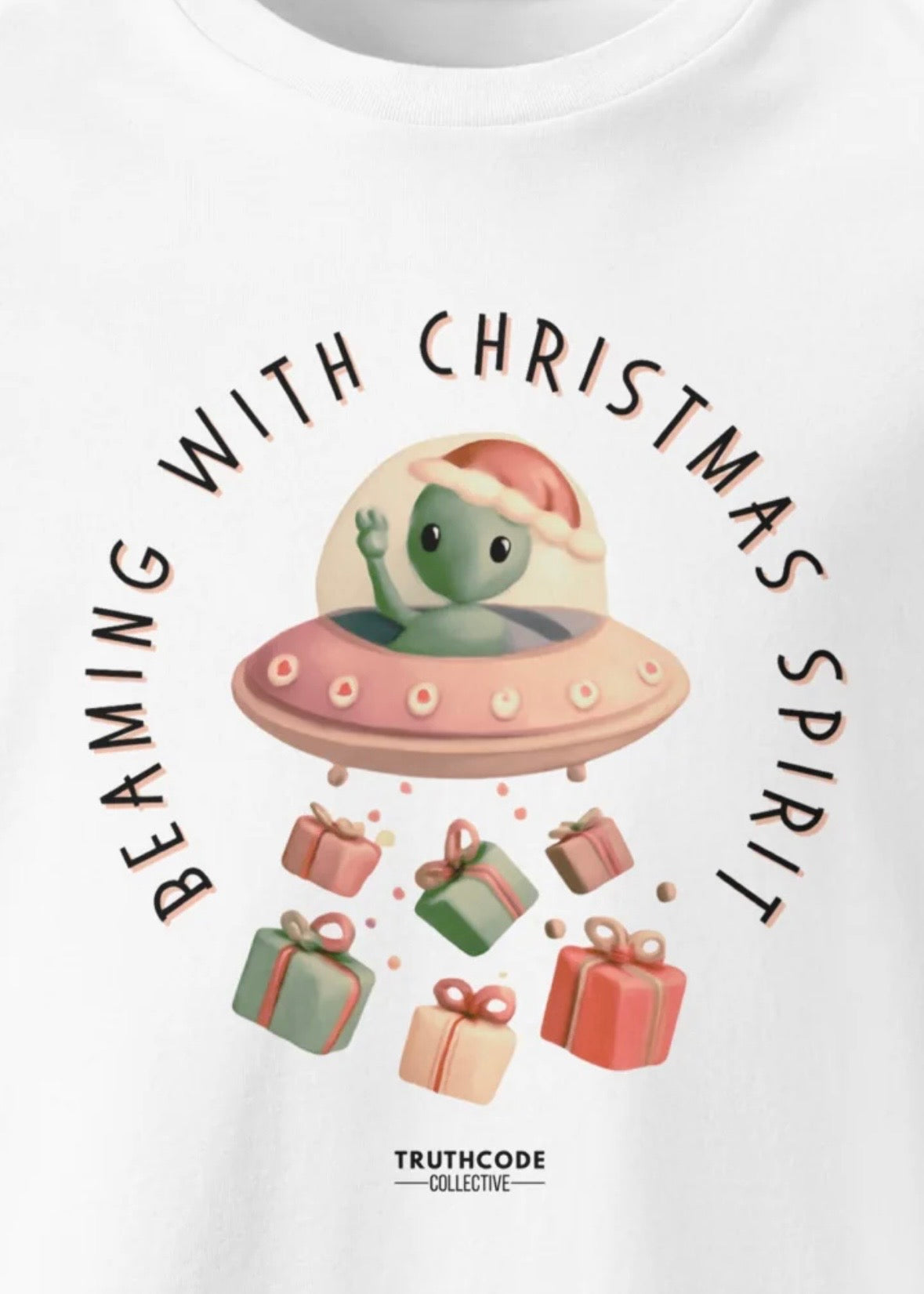 Close view of white organic t-shirt with cute alien in a spaceship Christmas-themed graphic and text 'Beaming with Christmas spirit'