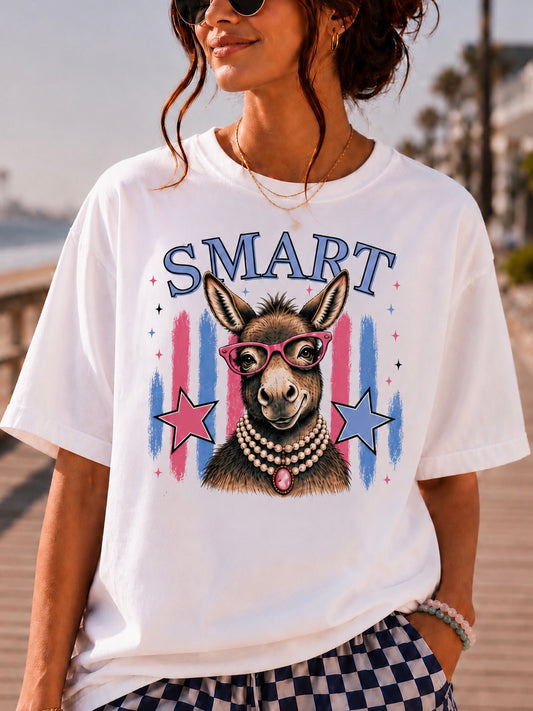 A woman wearing a white graphic t-shirt with a donkey illustration and the word 'SMART' in blue, paired with blue and white checkered shorts, set against a blurred outdoor background.