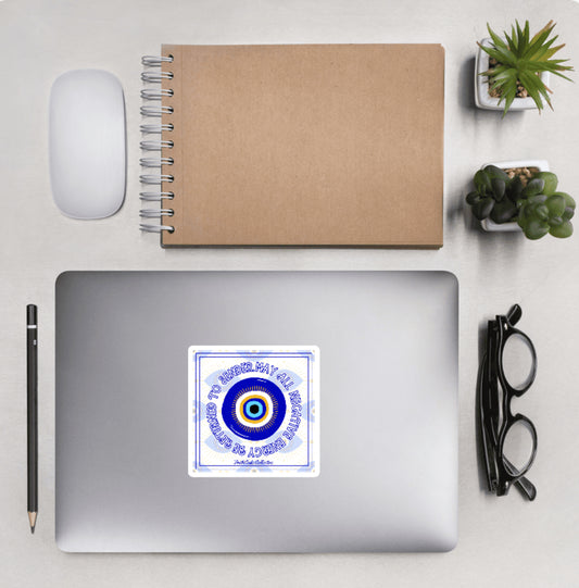 Aerial view of a desktop with laptop showing a squared sticker with eye design and text 'May all negative energy be returned to sender' on a white background