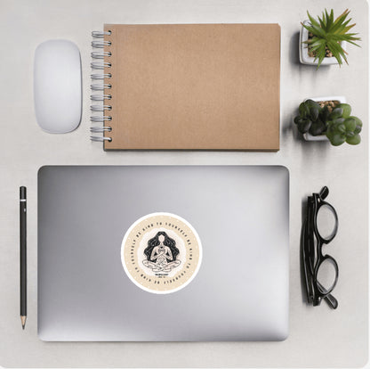 Aerial view of a desktop with laptop showing a circular sticker of a meditating woman and text 'Be kind to yourself' 