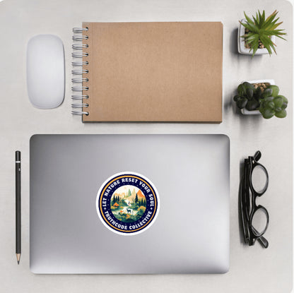 Aerial view of a desktop with laptop showing a circular sticker with a mountain scene and text 'Let nature reset your soul'