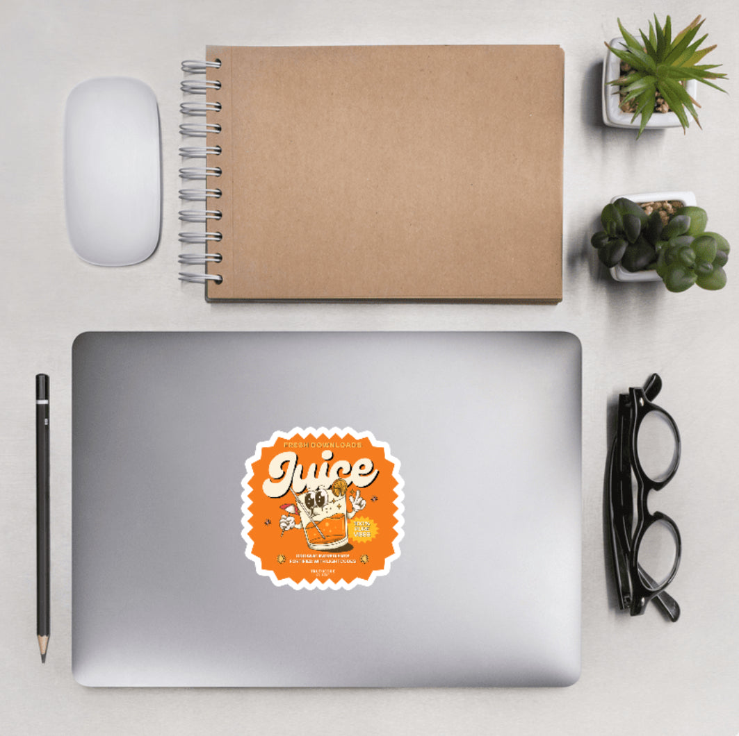 Aerial view of a desktop with laptop showing a sticker with a cartoon juice glass graphic and text 'Juice, fresh downloads, organic ingredients fortified with lightcodes'