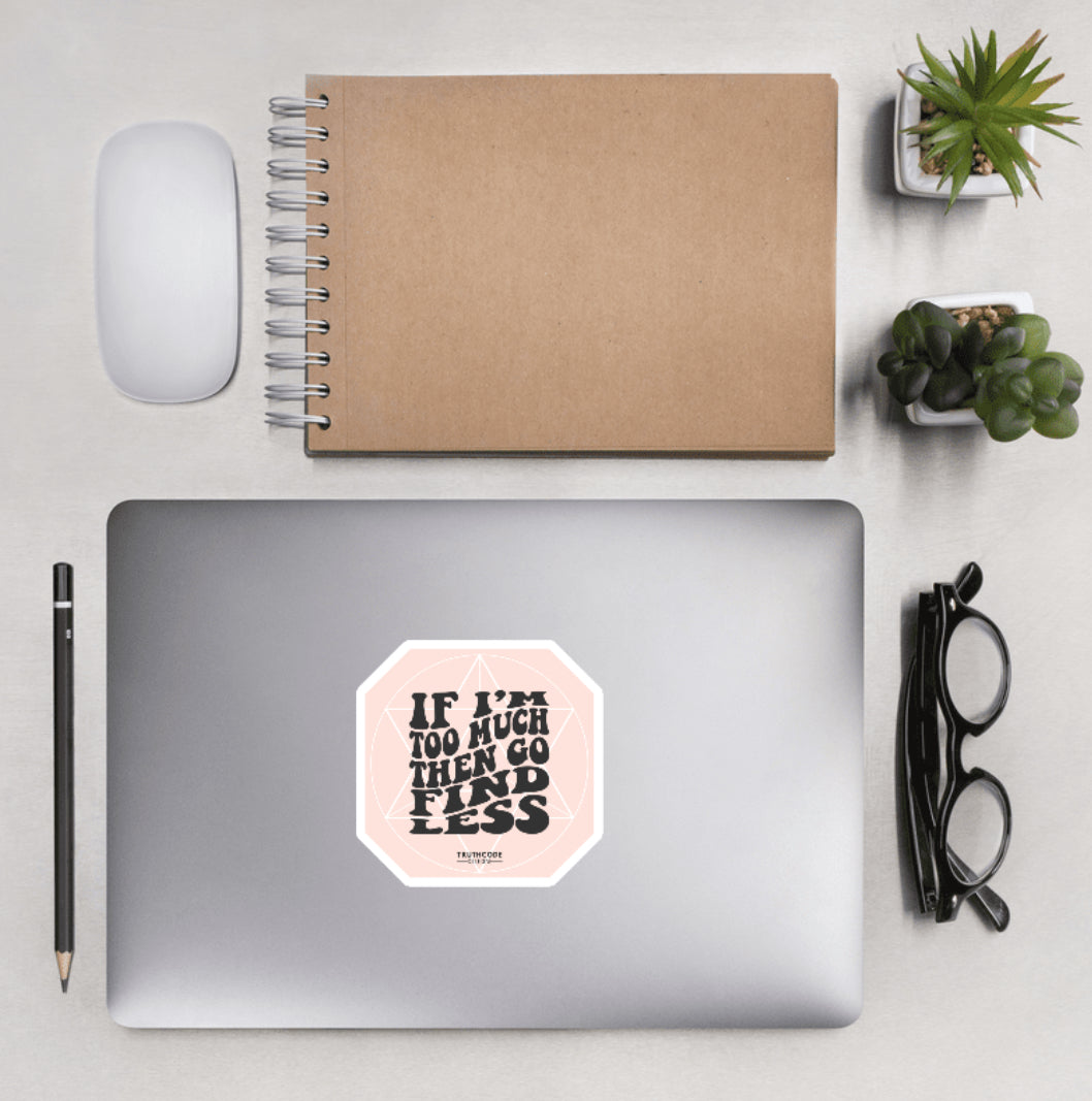 Aerial view of a desktop with laptop showing a light pink sticker with subtle geometric background design text 'If I'm too much then go find less' 