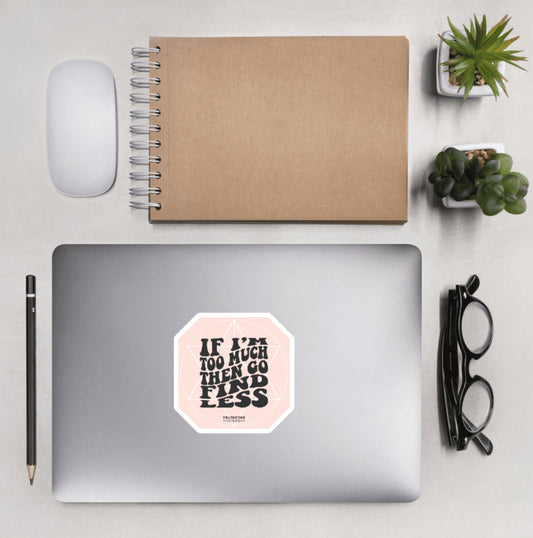 Aerial view of a desktop with laptop showing a light pink sticker with subtle geometric background design text 'If I'm too much then go find less' 