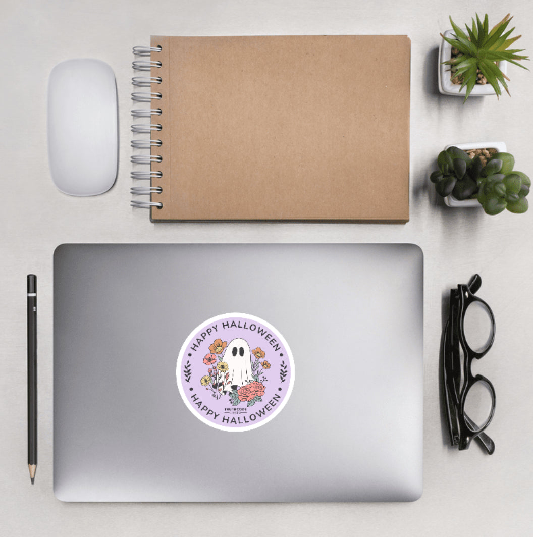 Aerial view of a desktop with laptop showing a circular sticker with cartoon ghost and floral design and text 'Happy Halloween'