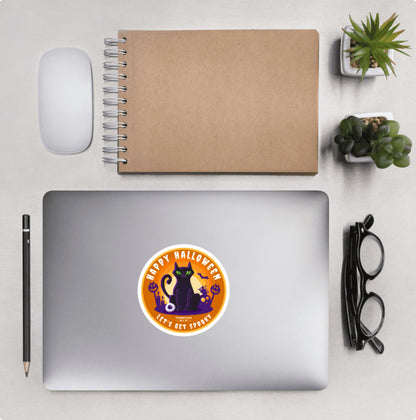 Aerial view of a desktop with laptop showing a circular sticker with black cat design and text 'Happy Halloween, let's get spooky'