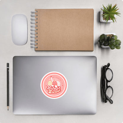 Aerial view of a desktop with laptop showing a circular sticker with ice cream design and text 'Life is sweet'