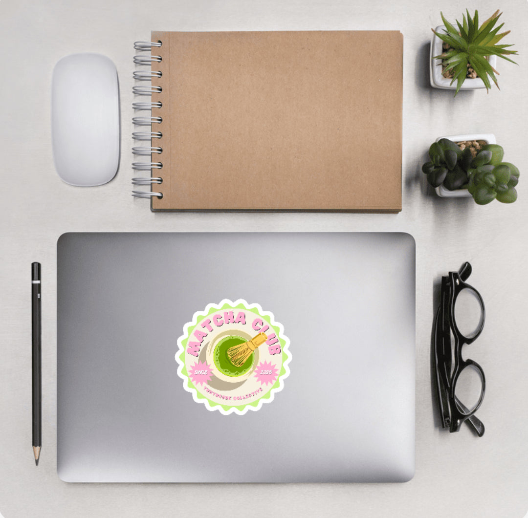 Aerial view of a desktop with laptop showing a circular scalloped sticker with graphic of a green drink and text 'Matcha club' 