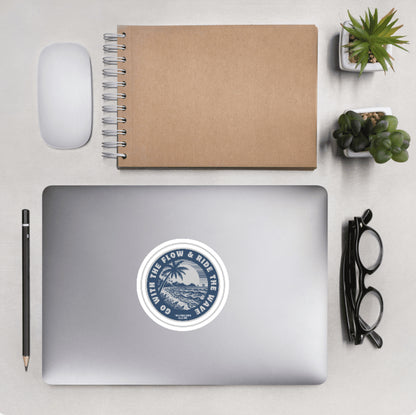 Aerial view of a desktop with laptop showing a circular sticker with a palm tree and ocean design and text 'Go with the flow & ride the wave' 