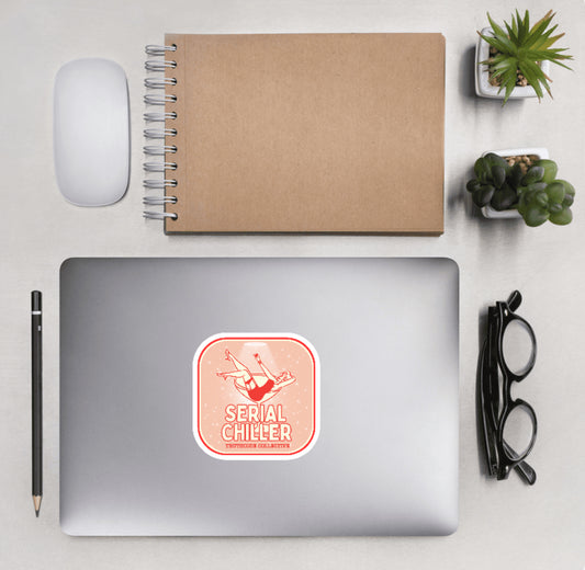 Aerial view of a desktop with laptop showing a squared sticker with a woman lying in a martini glass and text 'Serial Chiller'