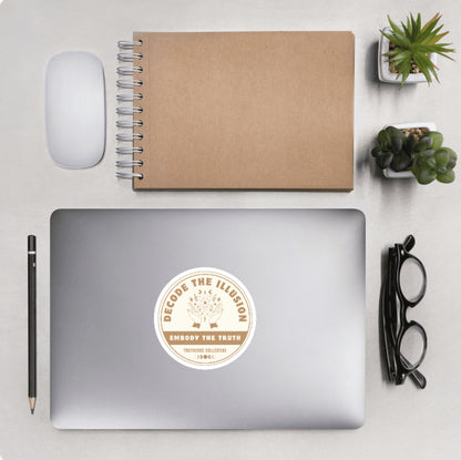 Aerial view of a desktop with laptop showing a circular sticker with design of hands and magic symbols and text 'Decode the illusion, embody the truth'
