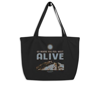 Black organic tote bag with motivational quote 'Go where you feel most alive' and nature graphic on a white background
