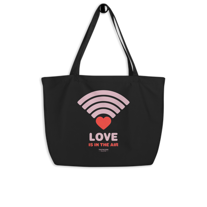 Black organic tote bag with pink heart wifi graphic design and text 'LOVE IS IN THE AIR' on a white background