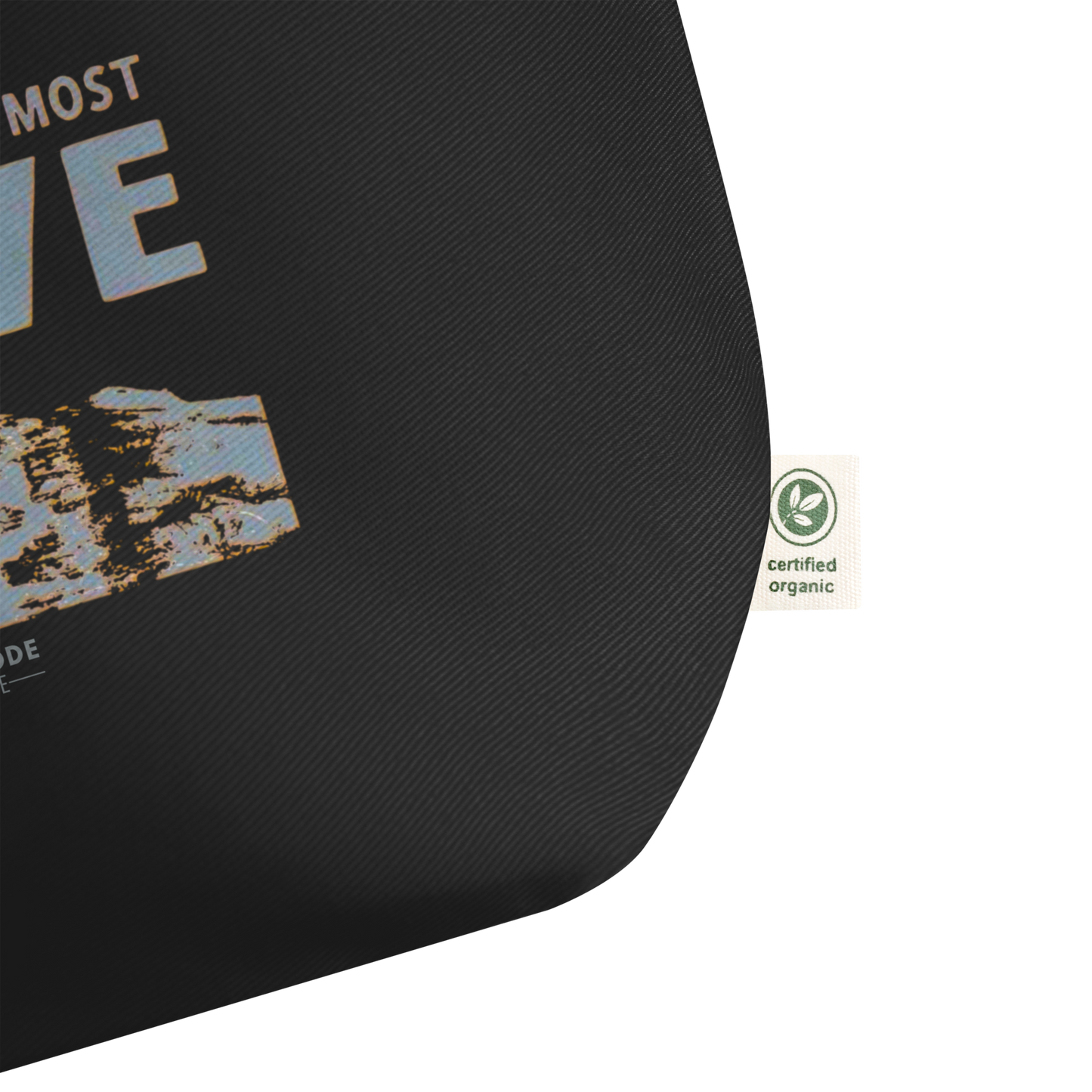 Black tote bag, zoomed in on a tag with text and a certified organic label on a white background 