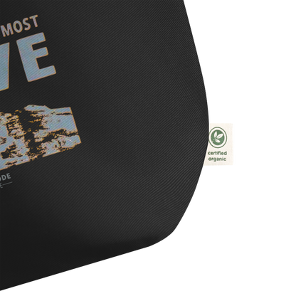 Black tote bag, zoomed in on a tag with text and a certified organic label on a white background 