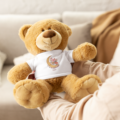 Tan teddy bear wearing a white shirt with a moon and flower design and text 'Take a moment to breathe', held by a person with a blurred background
