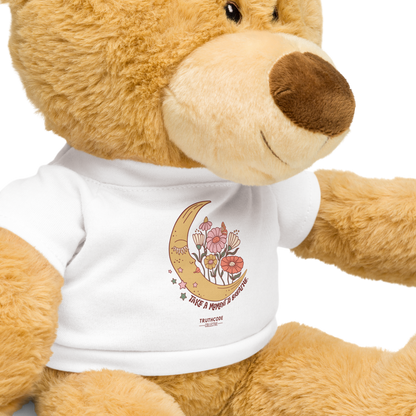 Close view of teddy bear wearing a white shirt with a moon and flower design and text 'Take a moment to breathe', on a white background