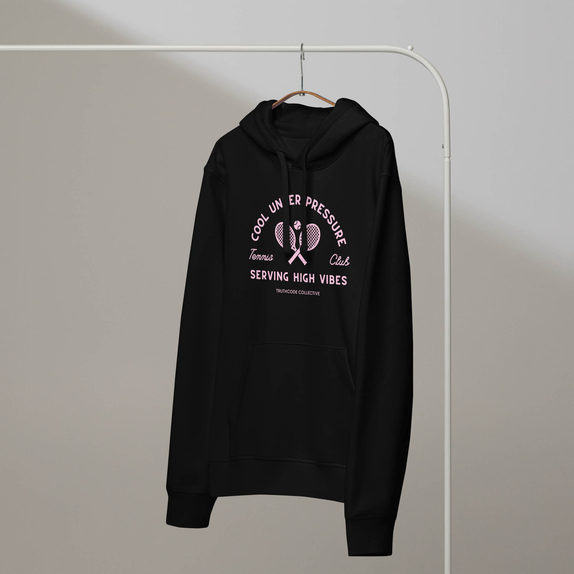 Black organic hoodie with text 'Cool under pressure, serving high vibes' and 'Tennis club' with a tennis racket design on a hanger with a gray wall background