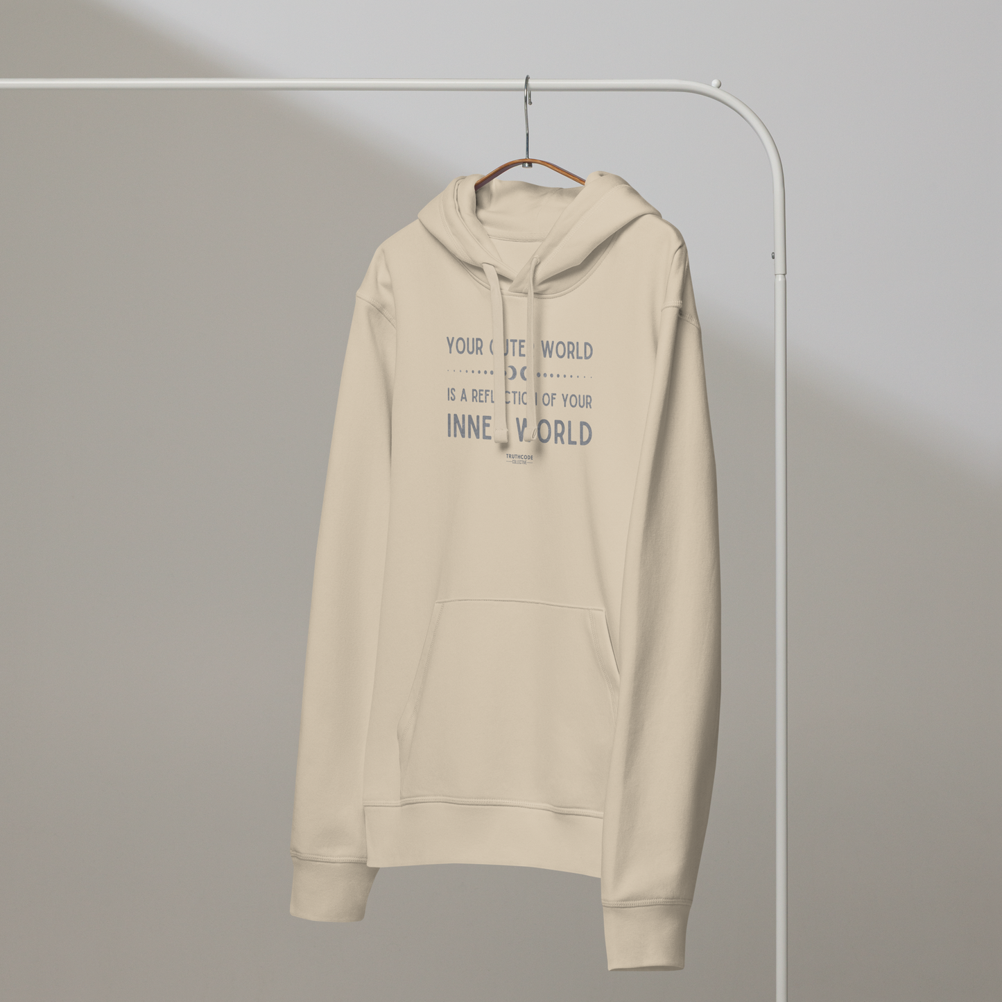 Beige organic hoodie with text 'Your outer world is a reflection of your inner world' on a white hanger with a gray wall background