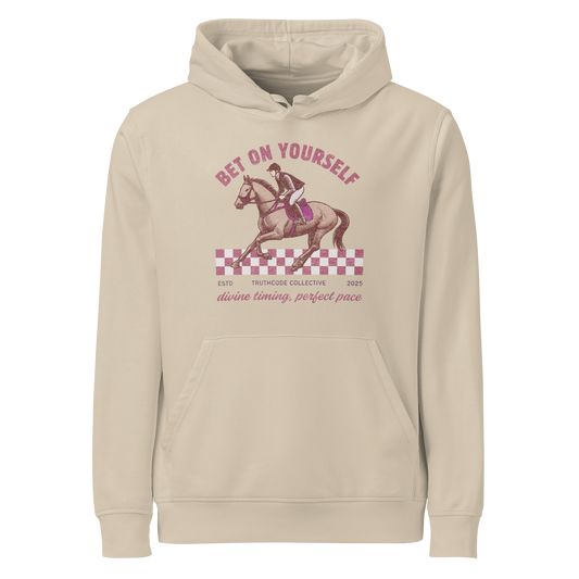 Beige organic hoodie with horse and rider graphic and text 'Bet on yourself, divine timing, perfect pace' on a white background