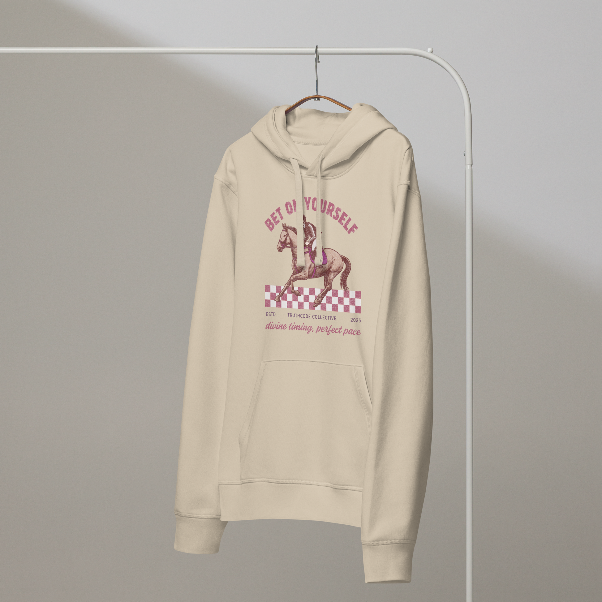 Beige organic hoodie with graphic design of race horse and jockey and text 'Bet on yourself' on a hanger with a plain background