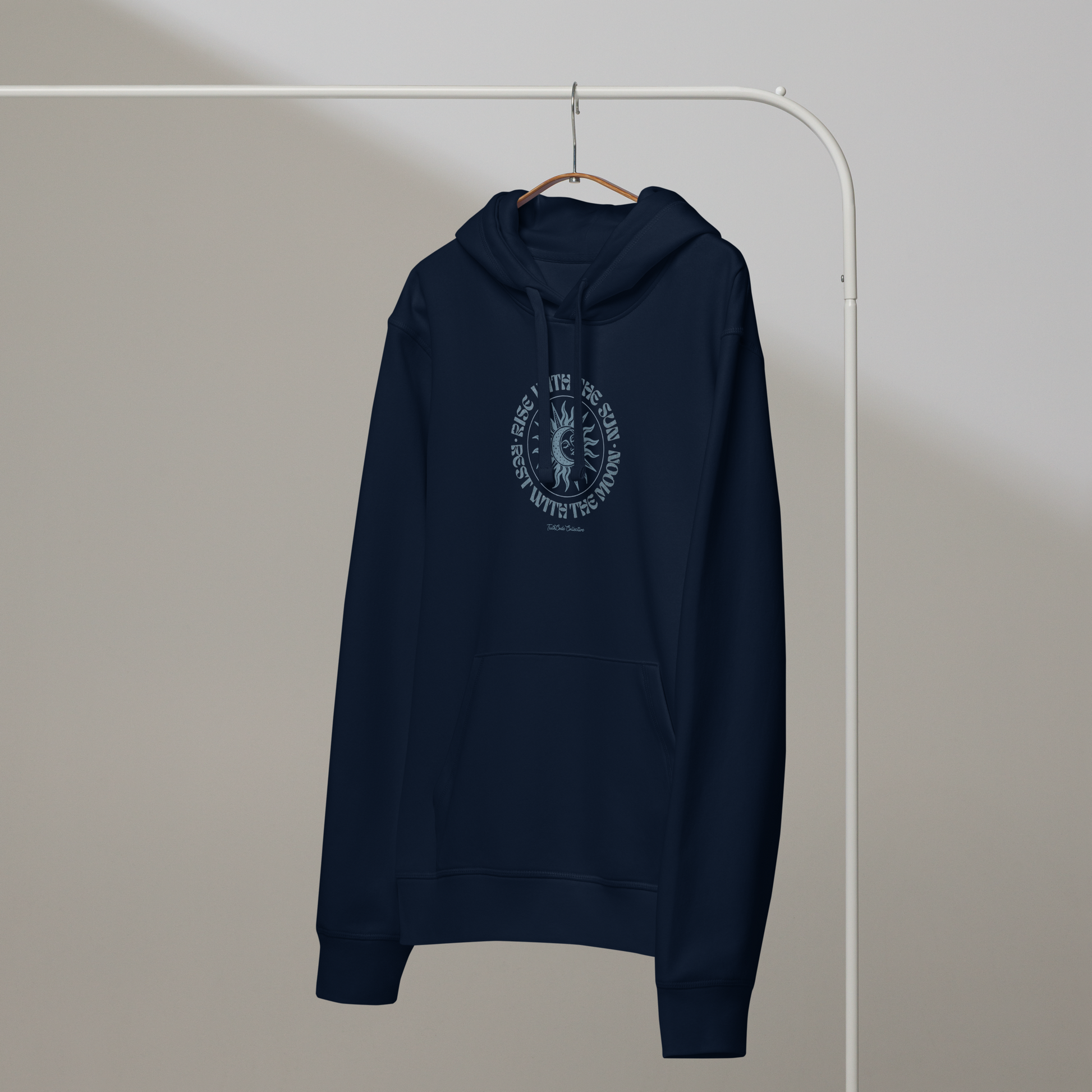 Navy blue organic hoodie with a circular sun/moon design and text 'Rise with the sun, rest with the moon' on a hanger against a plain background