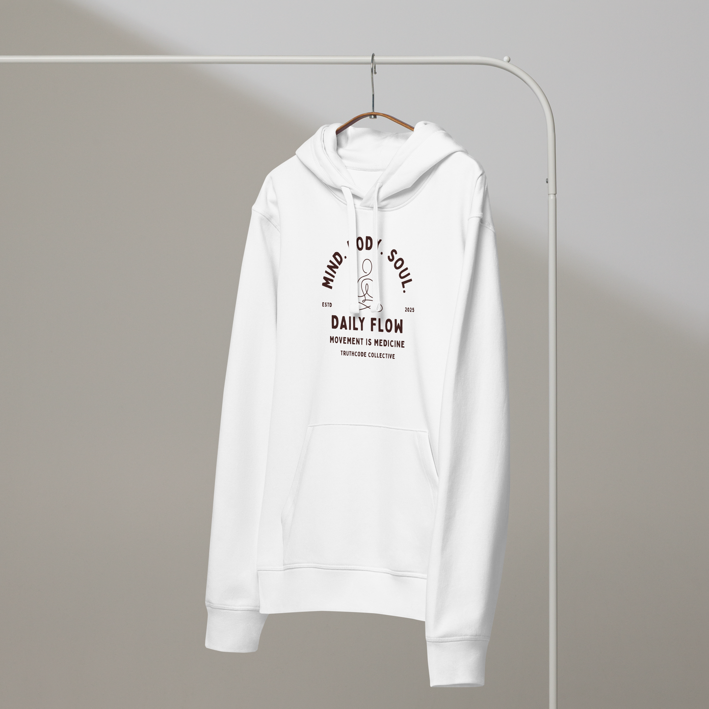 White organic hoodie with 'Daily Flow, movement is medicine' and 'Mind. Body. Soul' text and a line drawing graphic of a person meditating, on a white hanger with a grey wall background