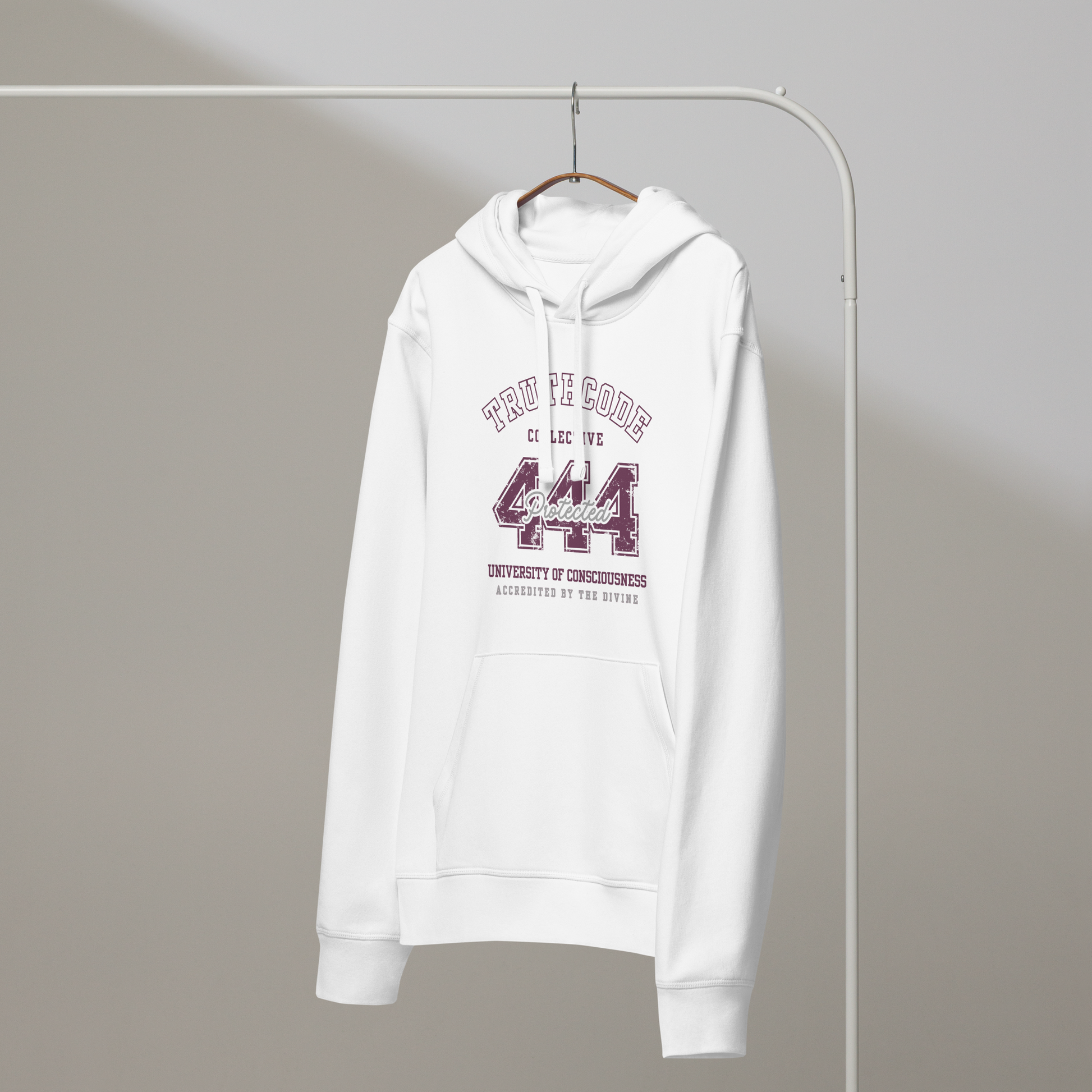 White organic hoodie with maroon text '444, protected' and 'University of consciousness, accredited by the divine'  on a white hanger with a gray wall background