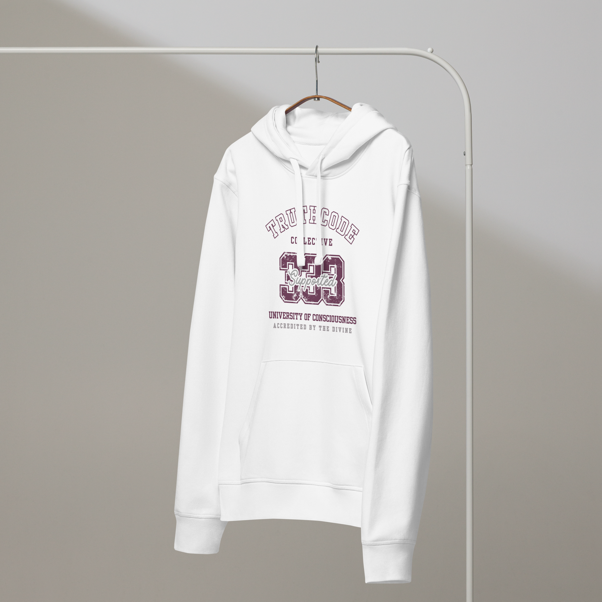 White organic hoodie with maroon text '333, Supported' and 'University of consciousness, accredited by the divine'  on a white hanger with a gray wall background