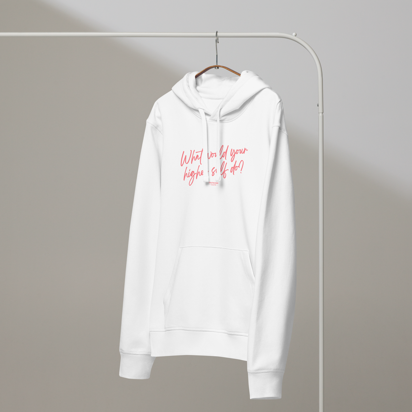 White organic hoodie with pink text 'What would your higher self do?' on a white hanger with a gray wall background