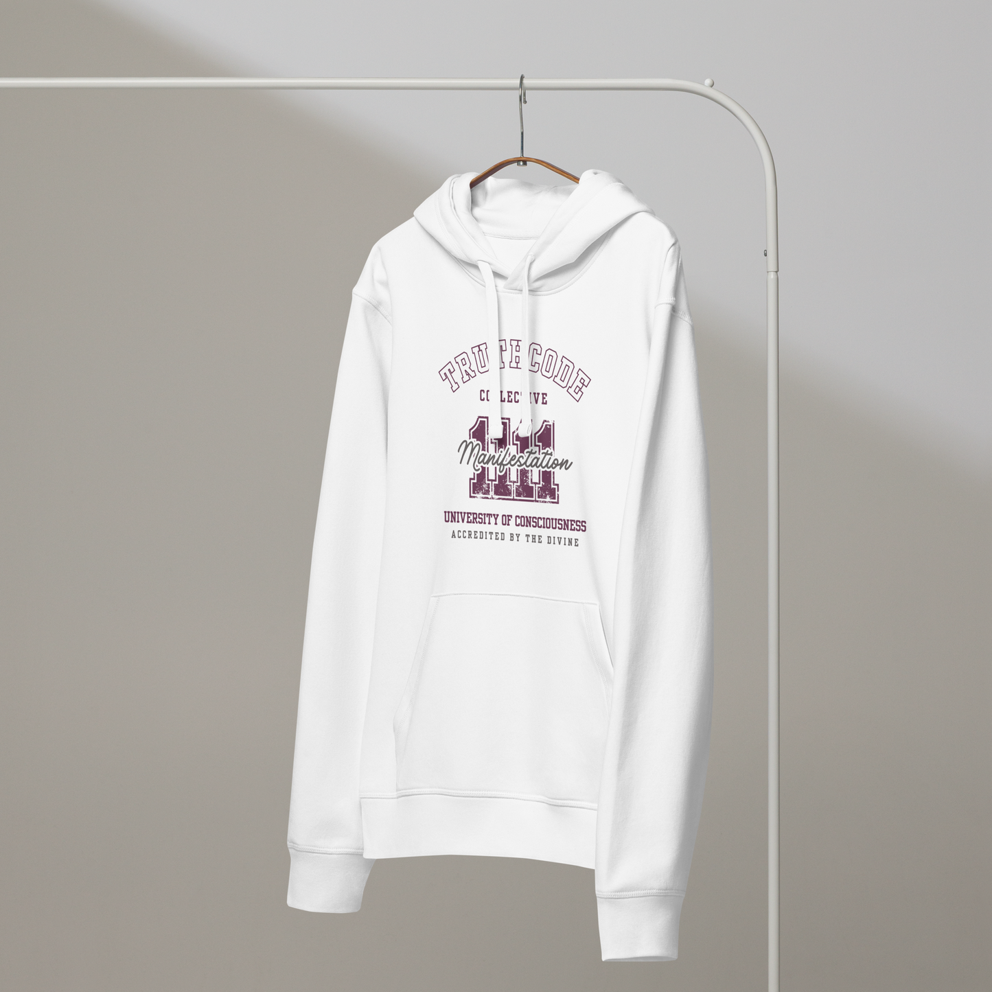 White organic hoodie with text design '1111 Manifestation' and 'University of Consciousness'  on a hanger with a gray wall background