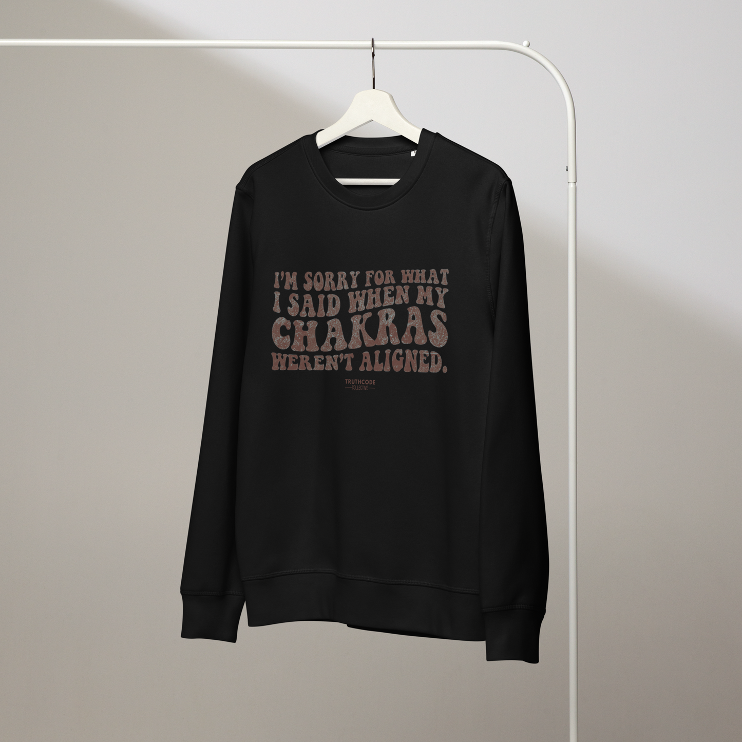 Black organic sweatshirt with text 'I'm sorry for what I said when my chakras weren't algined' on a hanger against a plain background