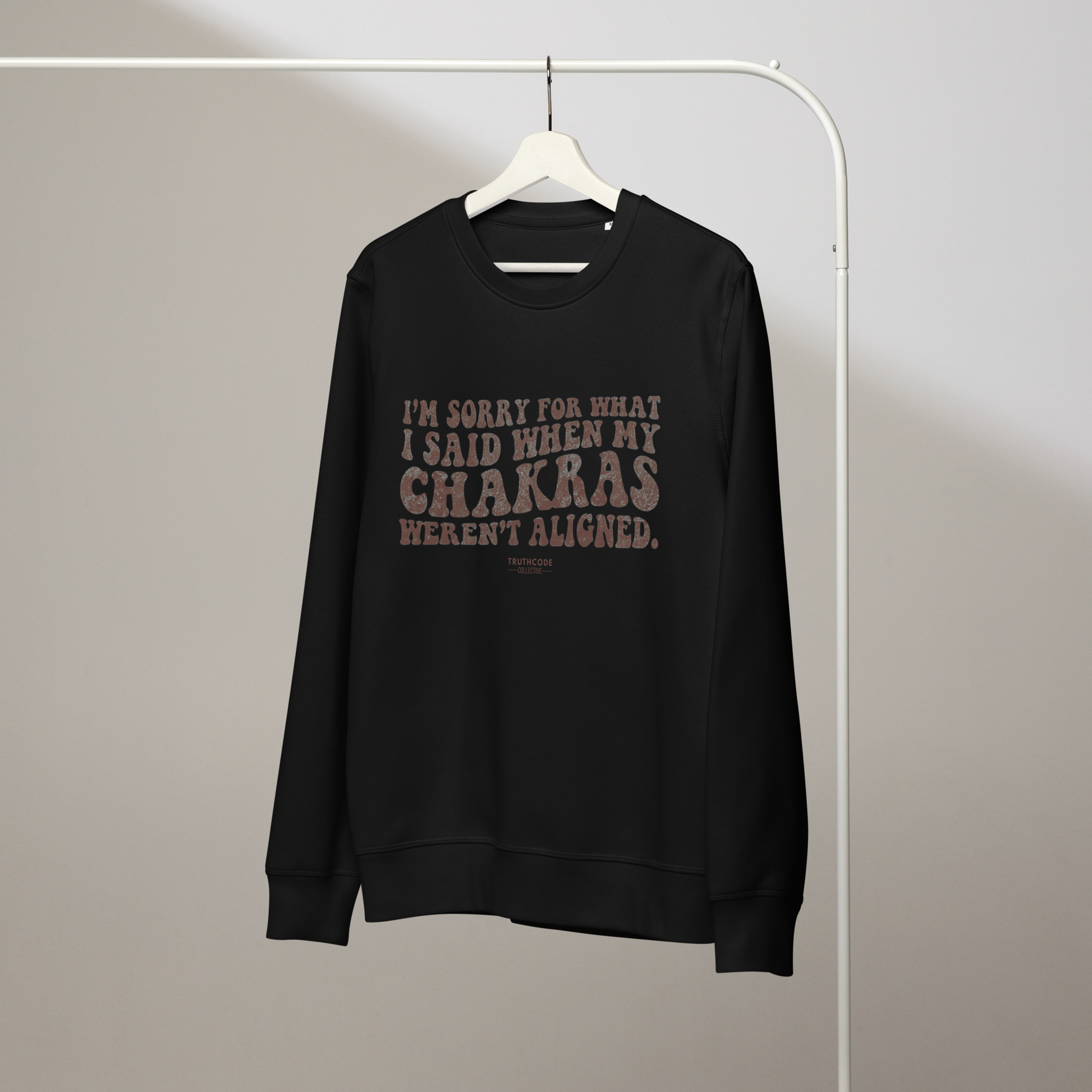 Black organic sweatshirt with text 'I'm sorry for what I said when my chakras weren't algined' on a hanger against a plain background