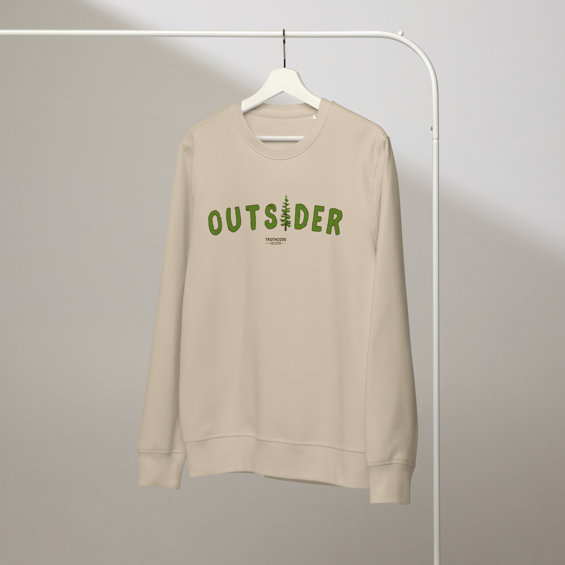 Beige organic sweatshirt with 'OUTSIDER' text and evergreen tree graphic on a white hanger with a gray wall background
