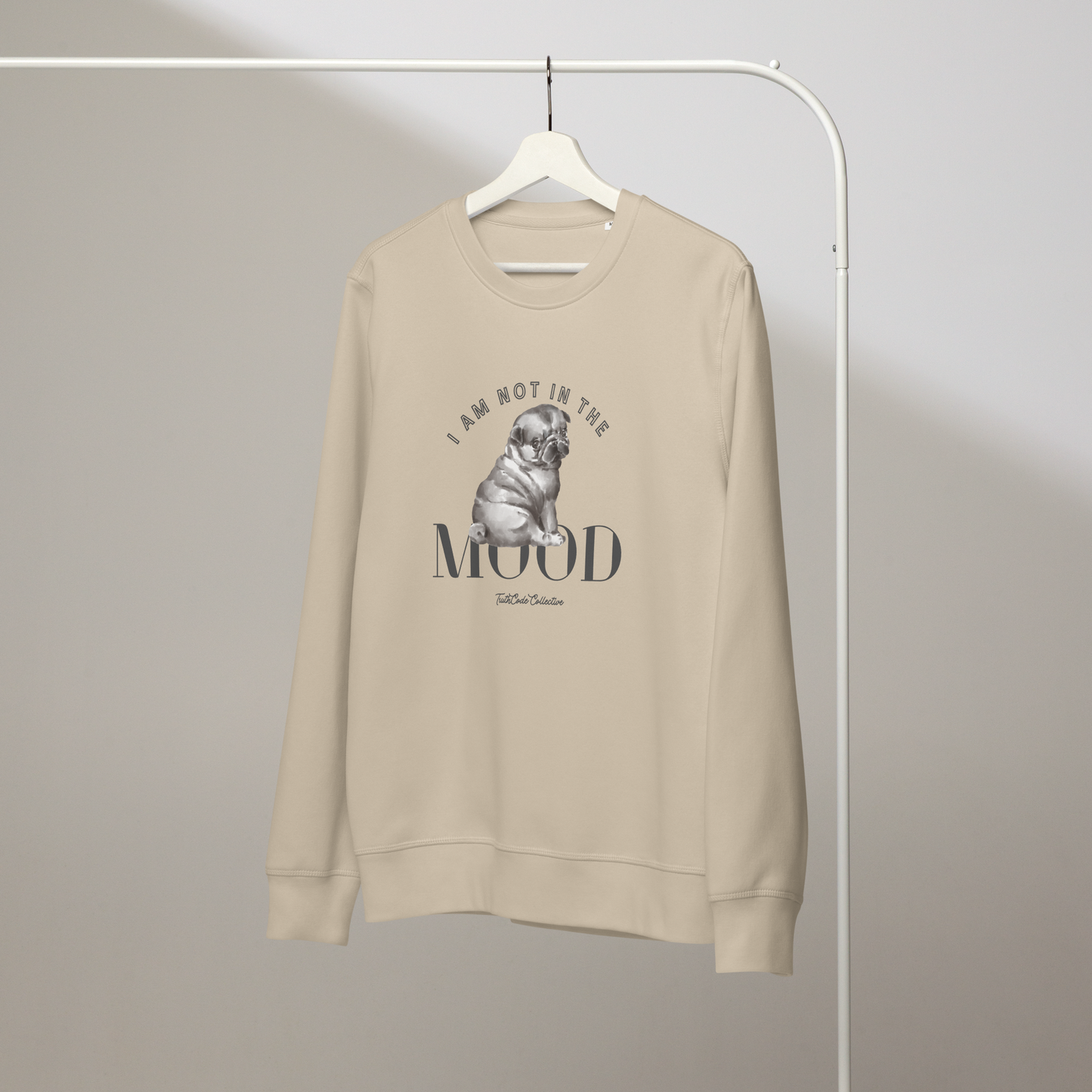 Beige organic sweatshirt with a pug graphic and text 'I am not in the mood' on a white hanger with a gray wall background