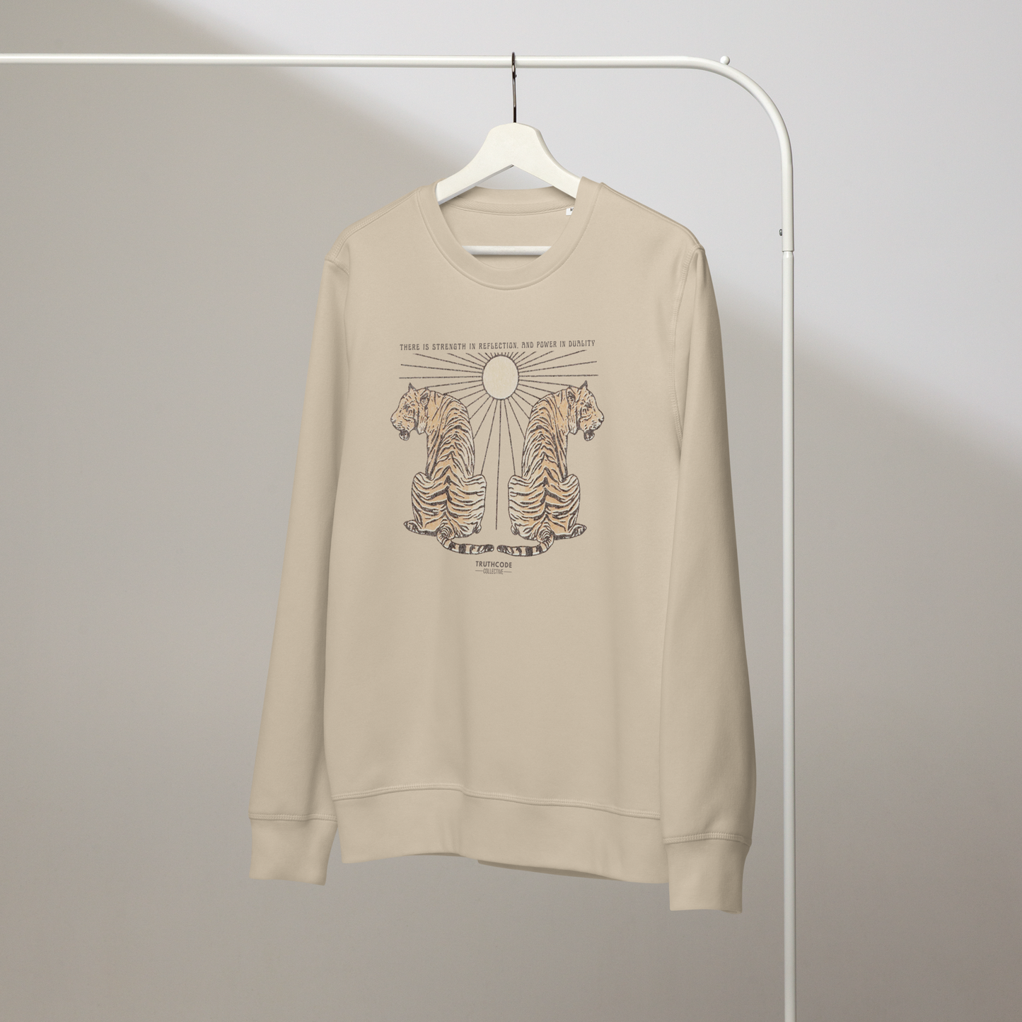 Beige organic sweatshirt with tiger design and text 'There is strength in reflection and power in duality'  on a white hanger with a gray wall background