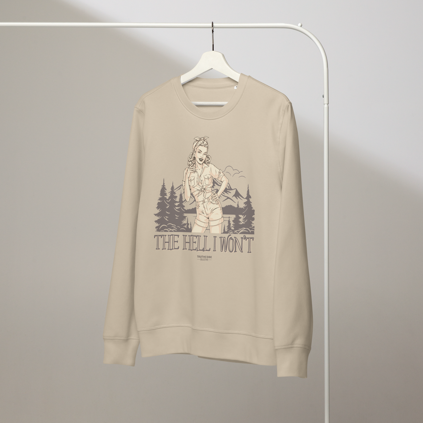 Beige organic sweatshirt with vintage graphic design of woman and a camping scene and text 'The hell I won't' on a white hanger with a gray wall background