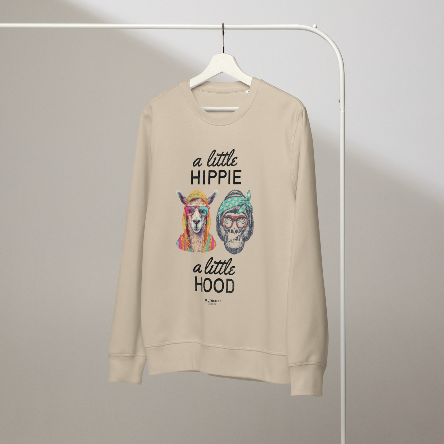 Beige organic sweatshirt with a graphic of a llama and monkey wearing headbands and text ' A little hippie, a little hood' on a white hanger with a plain wall background