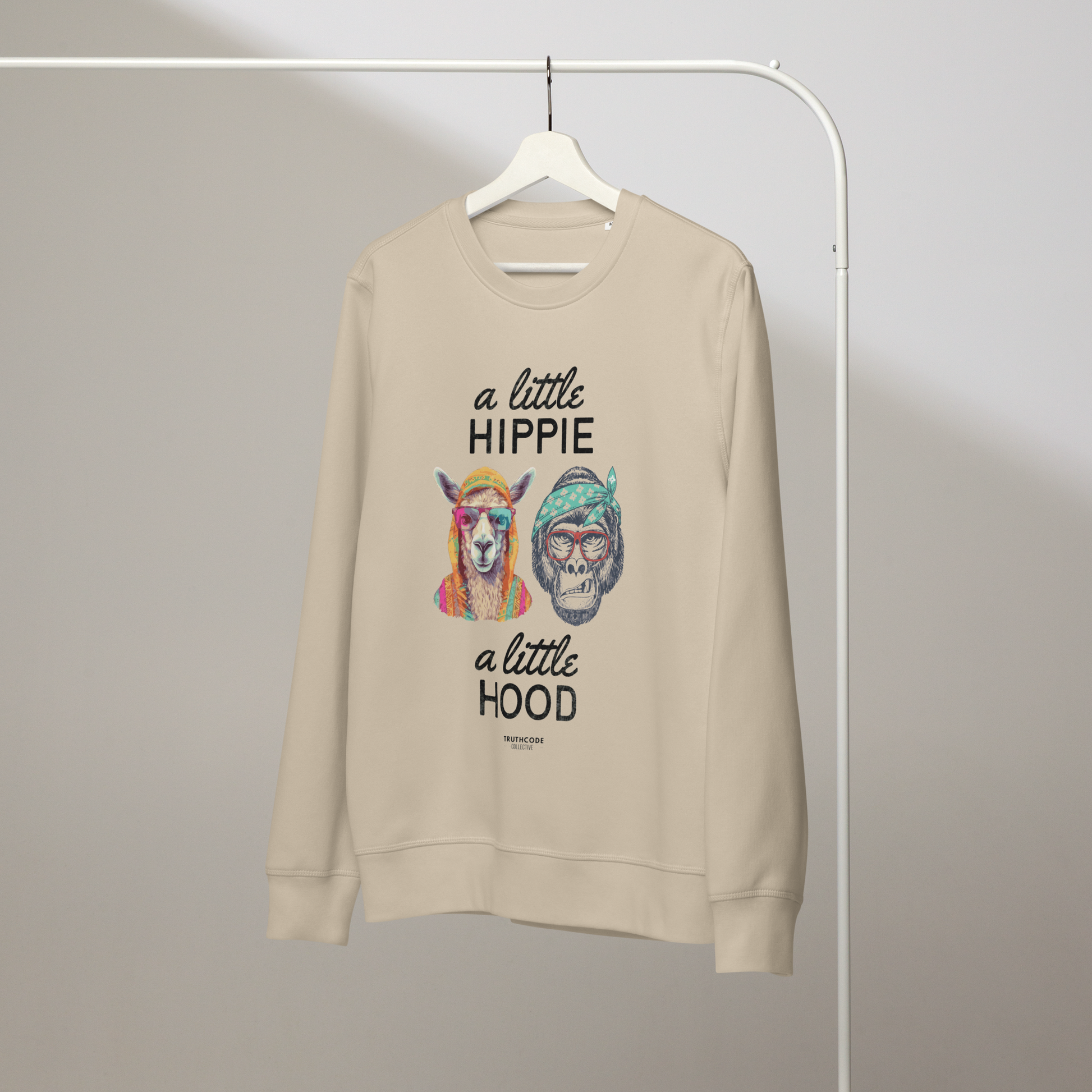 Beige organic sweatshirt with a graphic of a llama and monkey wearing headbands and text ' A little hippie, a little hood' on a white hanger with a plain wall background