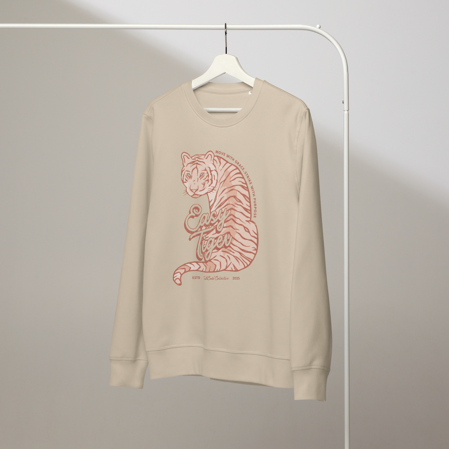 Beige organic sweatshirt with a tiger graphic and 'Easy Tiger' text on a white hanger with a gray wall background