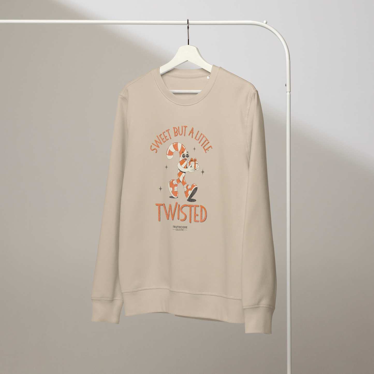 Beige organic sweatshirt with candy cane cartoon design and text 'Sweet but a little twisted' on a hanger against a plain background