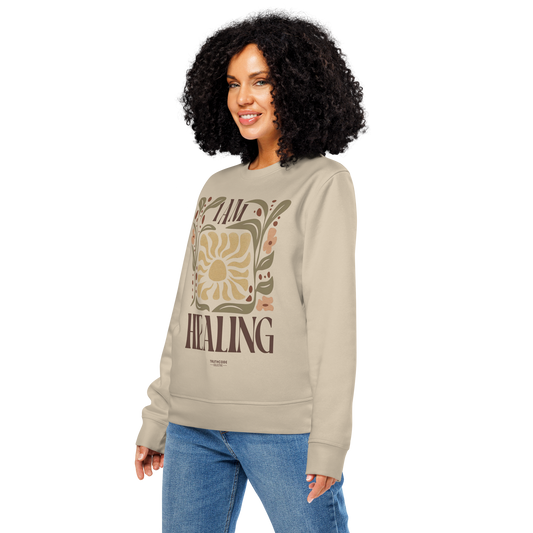 Woman wearing beige organic sweatshirt with 'I AM HEALING' text and sun and plants design on a white background
