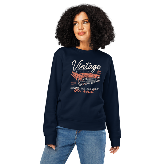 Woman wearing navy blue organic sweatshirt with vintage car graphic and text 'Vintage, reviving the legends of the road' on a white background