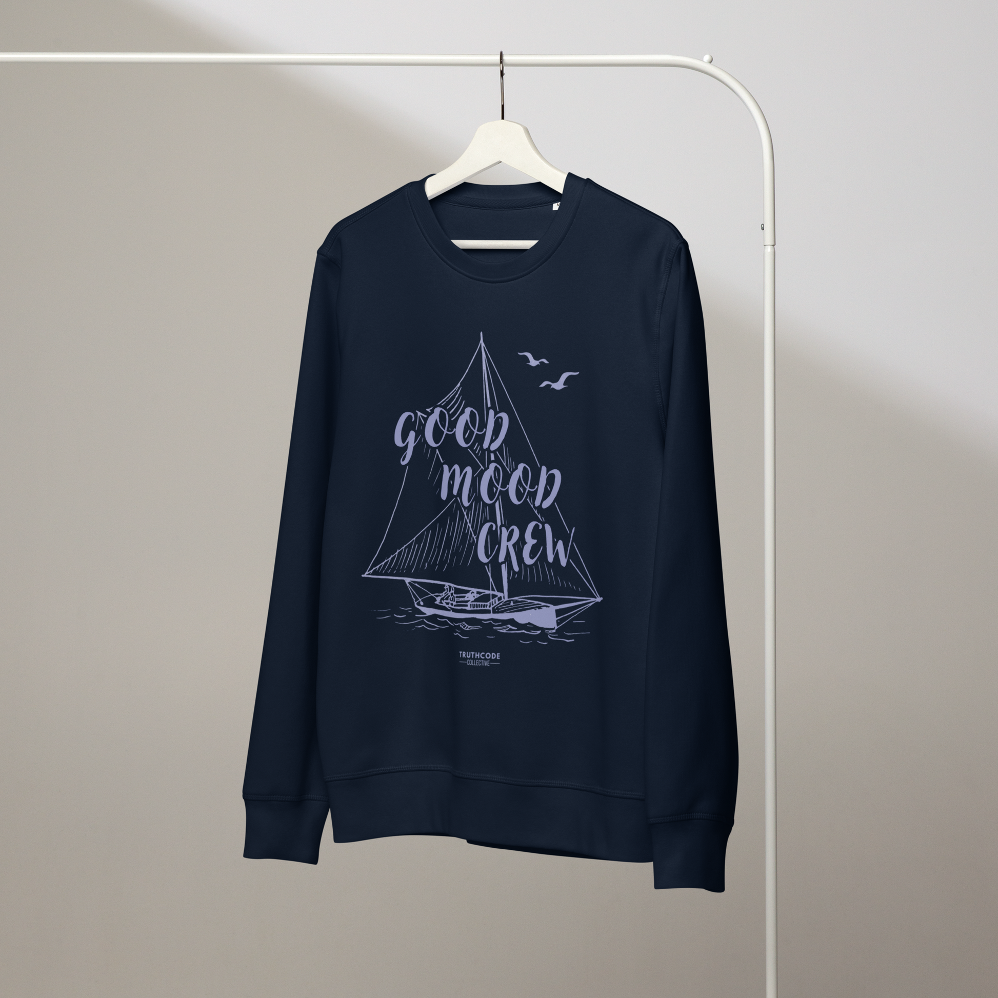 Navy blue organic sweatshirt with sailboat graphic and 'Good Mood Crew' text on a white hanger with a gray wall background
