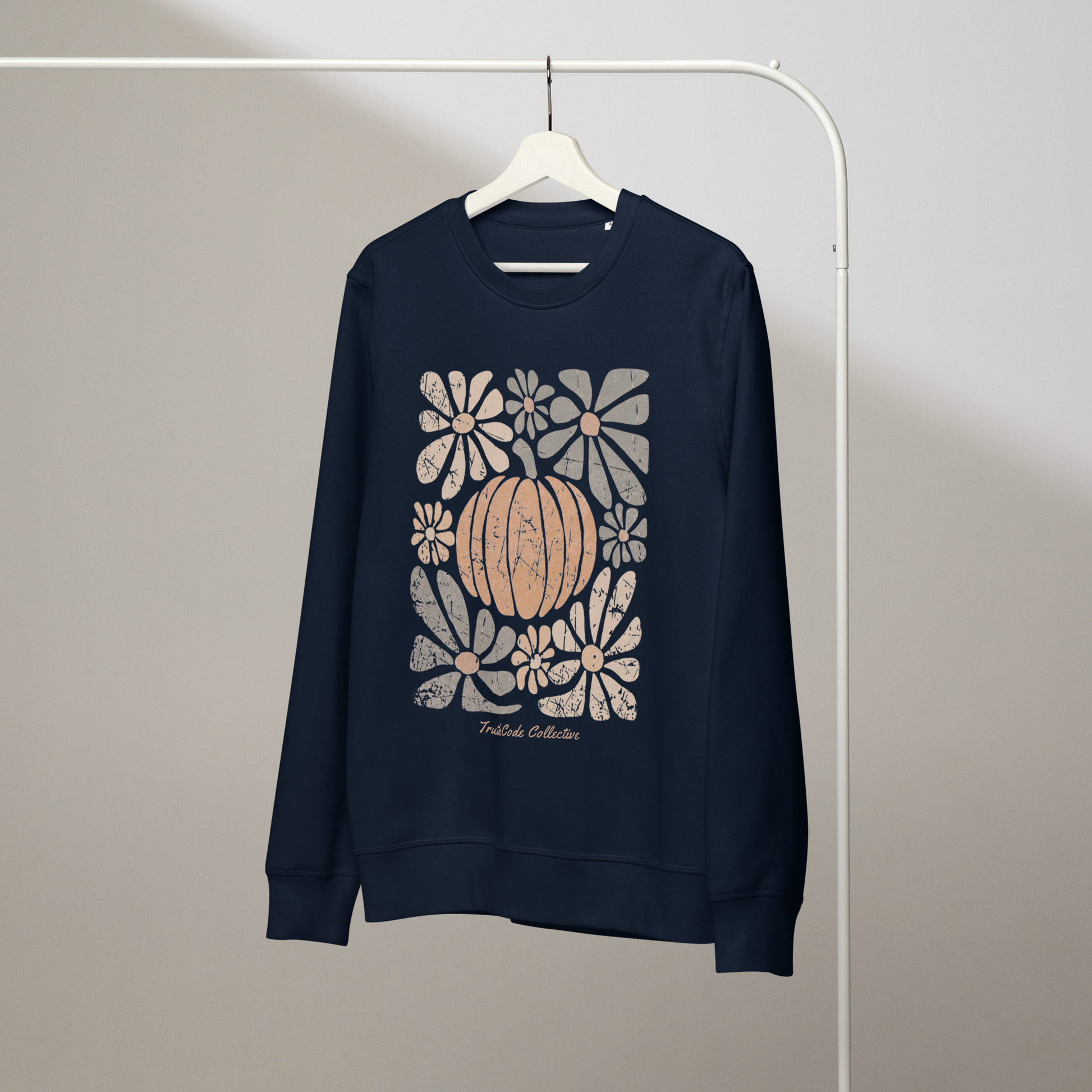 Navy blue organic sweatshirt with a pumpkin and floral design on a white hanger with a gray wall background