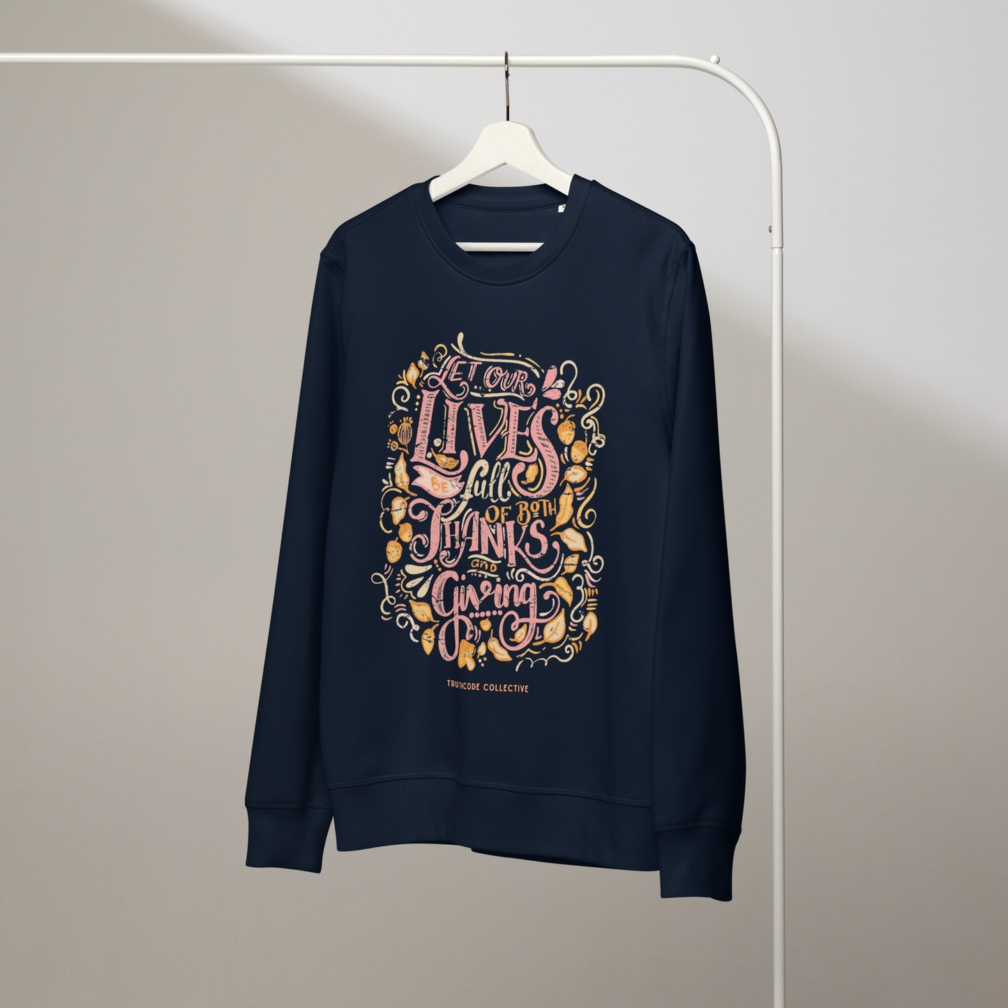 Navy blue organic sweatshirt with colorful text design 'Let our lives be full of both thanks and giving' on a white hanger with a gray wall background