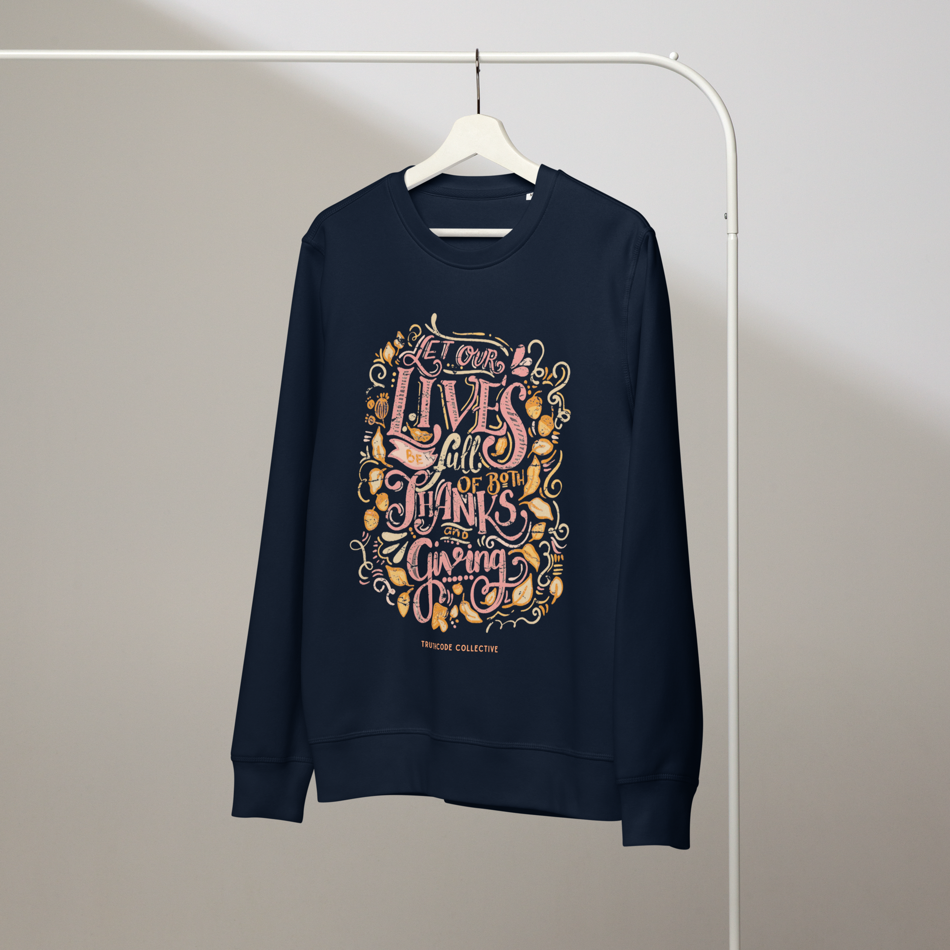 Navy blue organic sweatshirt with colorful text design 'Let our lives be full of both thanks and giving' on a white hanger with a gray wall background