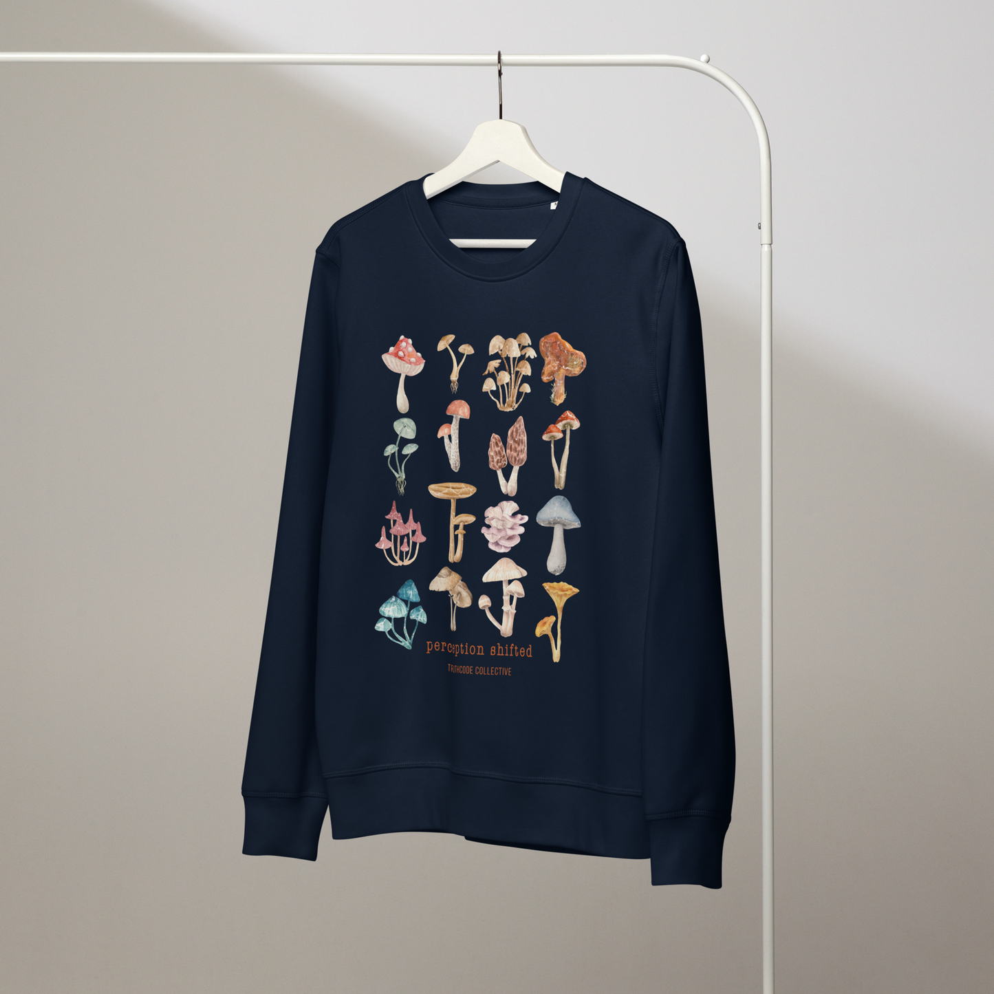 Navy blue organic sweatshirt with colorful mushroom illustrations and text 'Perception shifted' on a hanger with a gray wall background