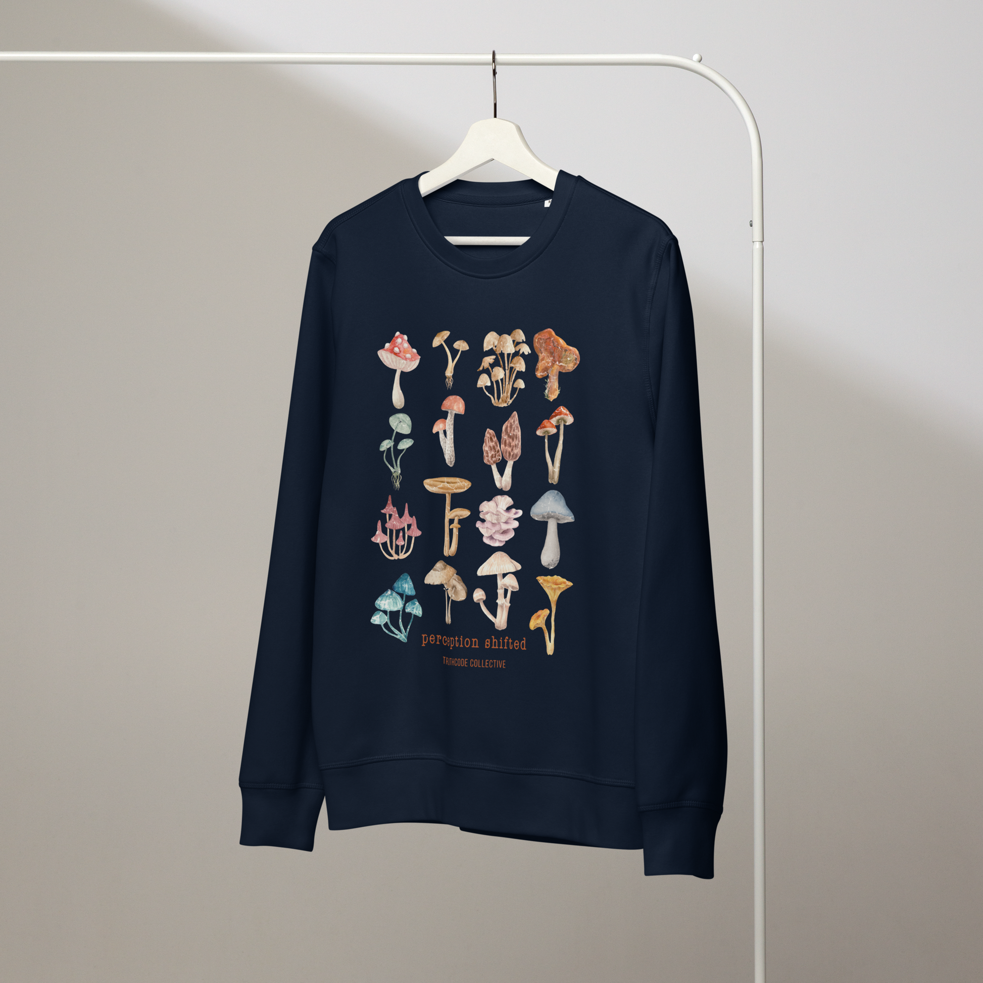 Navy blue organic sweatshirt with colorful mushroom illustrations and text 'Perception shifted' on a hanger with a gray wall background